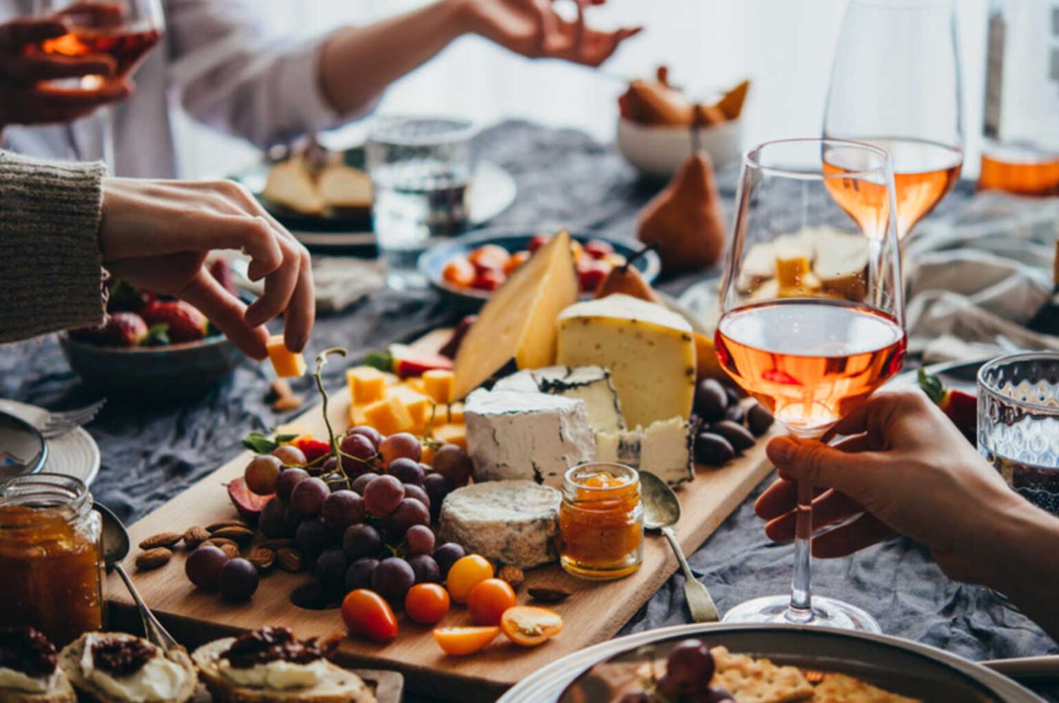 wine and cheese on a table with peoples hands holding glasses and food