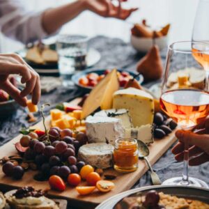 wine and cheese on a table with peoples hands holding glasses and food